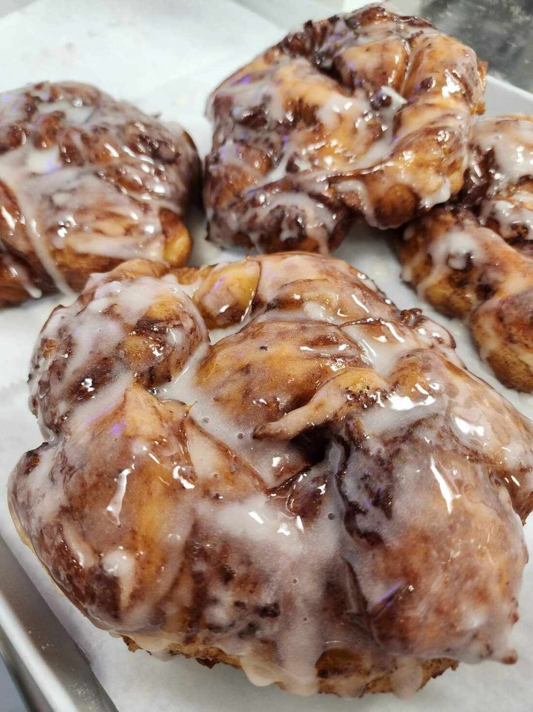 Freshly glazed apple fritters on a tray at The Cinnamon Bread Factory